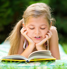 Image showing Little girl is reading a book outdoors