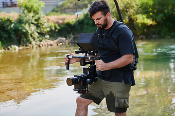 Image showing a professionally equipped cameraman shoots in the water surrounded by beautiful nature.