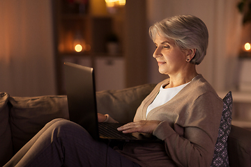 Image showing happy senior woman with laptop at home at night