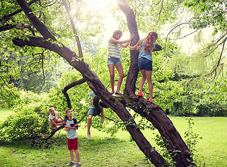 Image showing happy kids climbing up tree in summer park