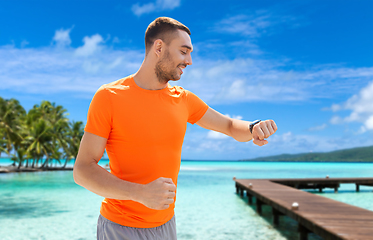 Image showing smiling man with smart watch running along beach