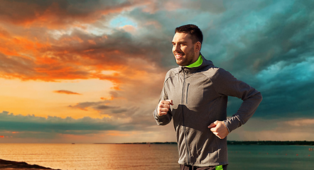 Image showing happy young man running over sea and sunset sky