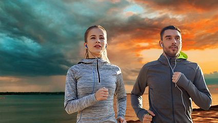 Image showing happy couple with earphones running over sea