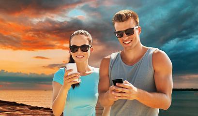 Image showing couple in sports clothes with smartphones on beach