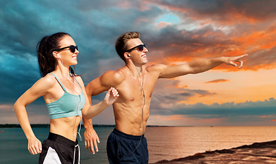 Image showing couple with earphones running along on beach