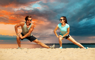 Image showing smiling couple stretching legs on beach