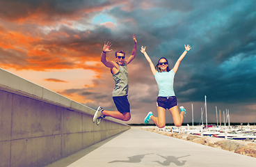 Image showing happy couple in sports clothes jumping on pier