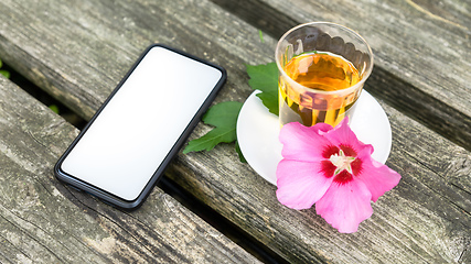 Image showing Mallow tea with smartphone on old wooden background