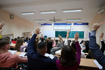Image showing Raised hands and arms of large group of people in class room