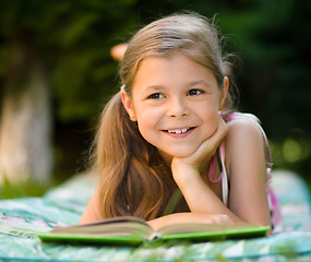 Image showing Little girl is reading a book outdoors