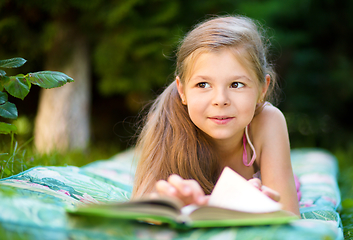 Image showing Little girl is reading a book outdoors