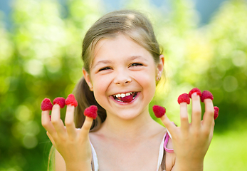 Image showing Young girl is holding raspberries on her fingers