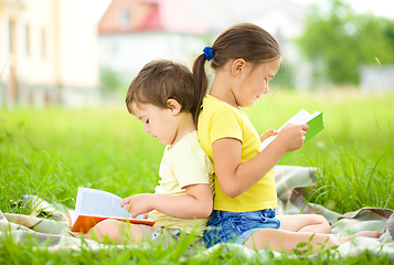 Image showing Little girl and boy are reading book outdoors