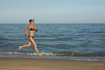 Image showing Sexy and happy beautiful woman in bikini running on the beach. In a cap with the inscription queen. Film effect.