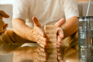 Image showing Close up of senior man\'s hands doing his wooden constructor at home - concept of home studying