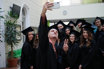 Image showing group of happy international students in mortar boards and bachelor gowns with diplomas taking selfie by smartphone