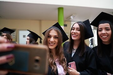 Image showing group of happy international students in mortar boards and bachelor gowns with diplomas taking selfie by smartphone