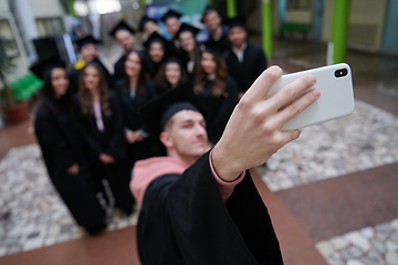 Image showing group of happy international students in mortar boards and bachelor gowns with diplomas taking selfie by smartphone