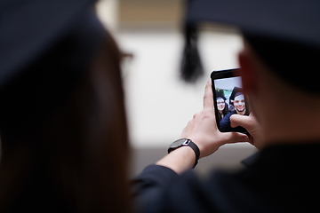 Image showing group of happy international students in mortar boards and bachelor gowns with diplomas taking selfie by smartphone