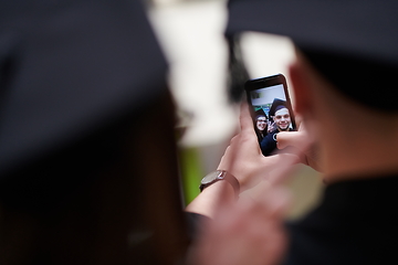 Image showing group of happy international students in mortar boards and bachelor gowns with diplomas taking selfie by smartphone