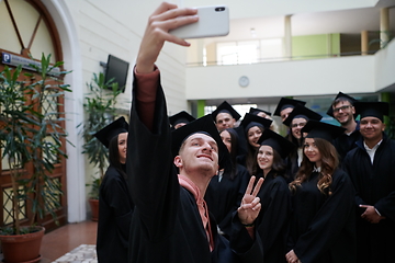 Image showing group of happy international students in mortar boards and bachelor gowns with diplomas taking selfie by smartphone