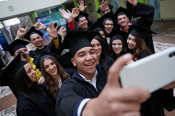 Image showing group of happy international students in mortar boards and bachelor gowns with diplomas taking selfie by smartphone