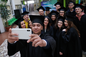 Image showing group of happy international students in mortar boards and bachelor gowns with diplomas taking selfie by smartphone