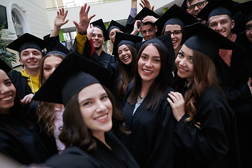 Image showing group of happy international students in mortar boards and bachelor gowns with diplomas taking selfie by smartphone