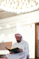 Image showing muslim man praying Allah alone inside the mosque and reading islamic holly book