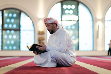 Image showing muslim man praying Allah alone inside the mosque and reading islamic holly book