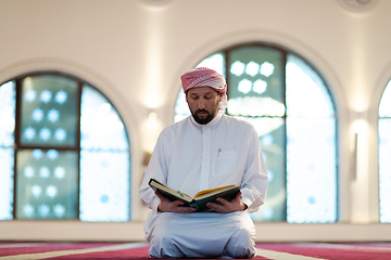 Image showing muslim man praying Allah alone inside the mosque and reading islamic holly book