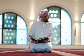 Image showing muslim man praying Allah alone inside the mosque and reading islamic holly book