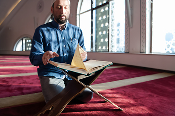 Image showing muslim man praying Allah alone inside the mosque and reading islamic holly book