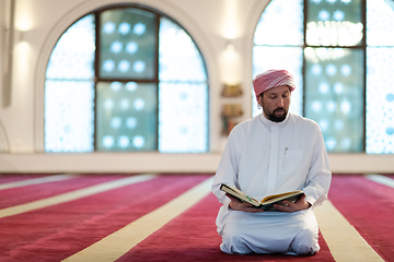 Image showing muslim man praying Allah alone inside the mosque and reading islamic holly book