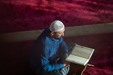 Image showing muslim man praying Allah alone inside the mosque and reading islamic holly book