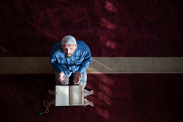 Image showing muslim man praying Allah alone inside the mosque and reading islamic holly book