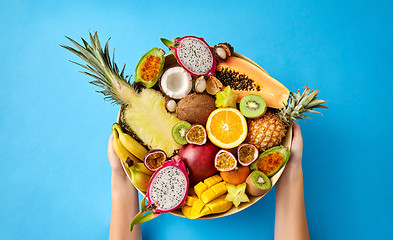 Image showing hands holding plate of exotic fruits over blue