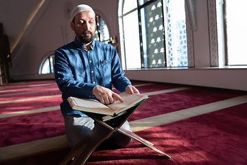 Image showing muslim man praying Allah alone inside the mosque and reading islamic holly book