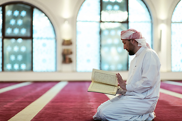 Image showing muslim man praying Allah alone inside the mosque and reading islamic holly book