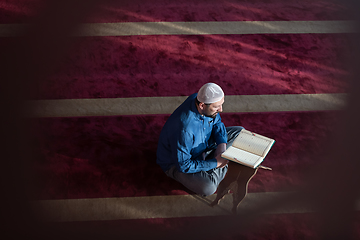 Image showing muslim man praying Allah alone inside the mosque and reading islamic holly book