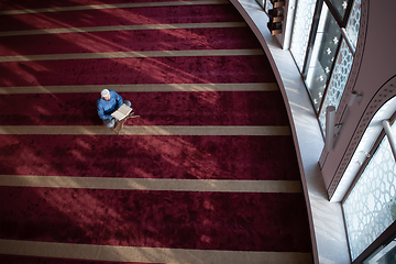 Image showing muslim man praying Allah alone inside the mosque and reading islamic holly book