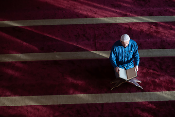 Image showing muslim man praying Allah alone inside the mosque and reading islamic holly book