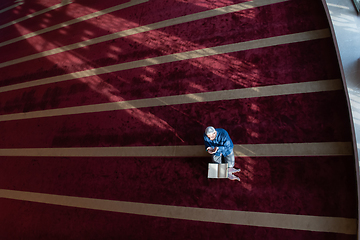 Image showing muslim man praying Allah alone inside the mosque and reading islamic holly book