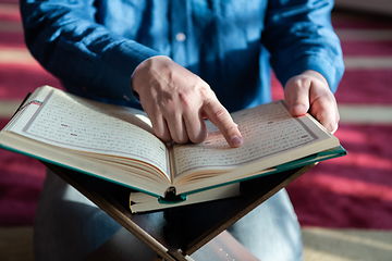 Image showing muslim man praying Allah alone inside the mosque and reading islamic holly book