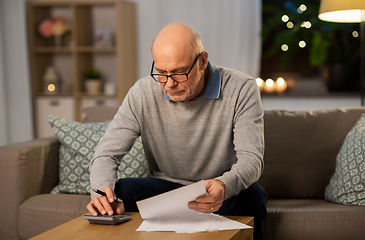 Image showing old man with bills counting on calculator at home