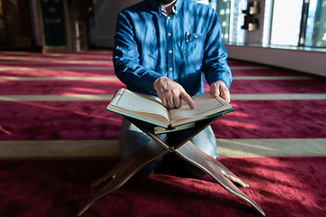 Image showing muslim man praying Allah alone inside the mosque and reading islamic holly book