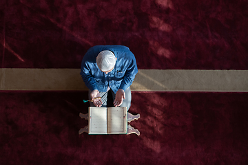 Image showing muslim man praying Allah alone inside the mosque and reading islamic holly book