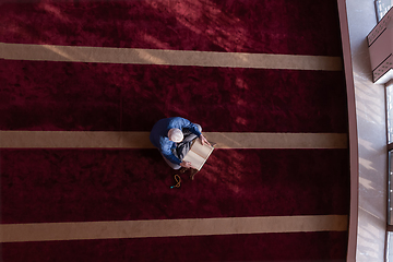 Image showing muslim man praying Allah alone inside the mosque and reading islamic holly book