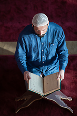 Image showing muslim man praying Allah alone inside the mosque and reading islamic holly book