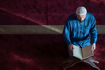 Image showing muslim man praying Allah alone inside the mosque and reading islamic holly book